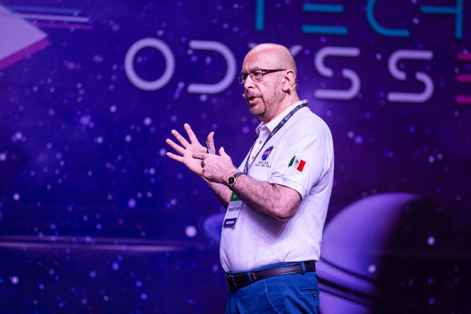 Speaker gesturing enthusiastically on tech conference stage with space-themed backdrop.