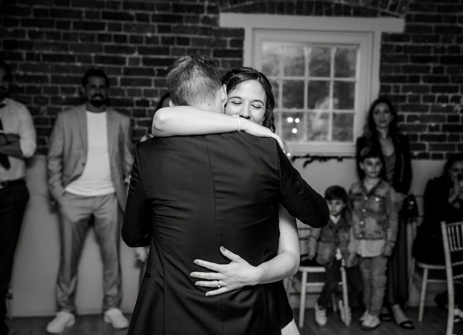 Wedding couple embraces during their first dance in front of exposed brick walls.