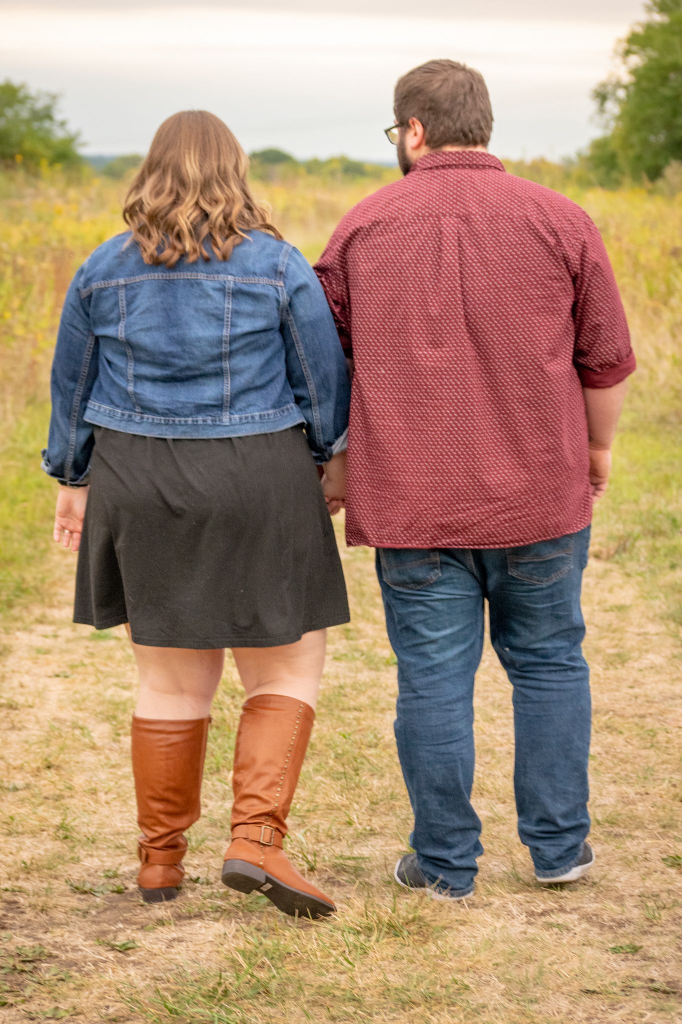 A couple walking hand-in-hand through a field in fall. Baby announcement session. Kansas City MO
