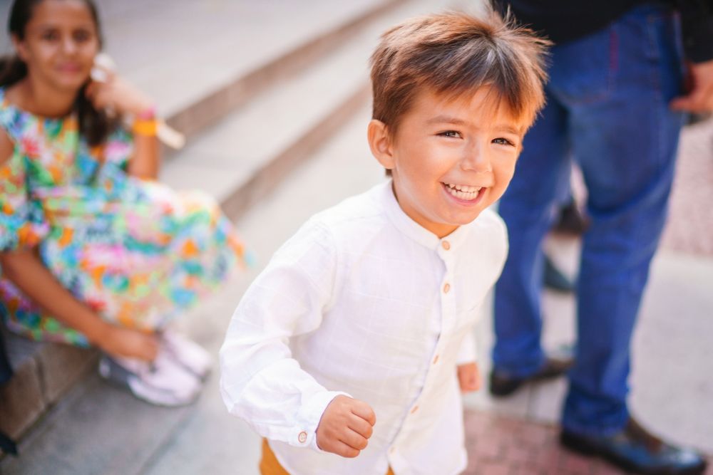 Young child in white clothing smiles and runs on a porch.