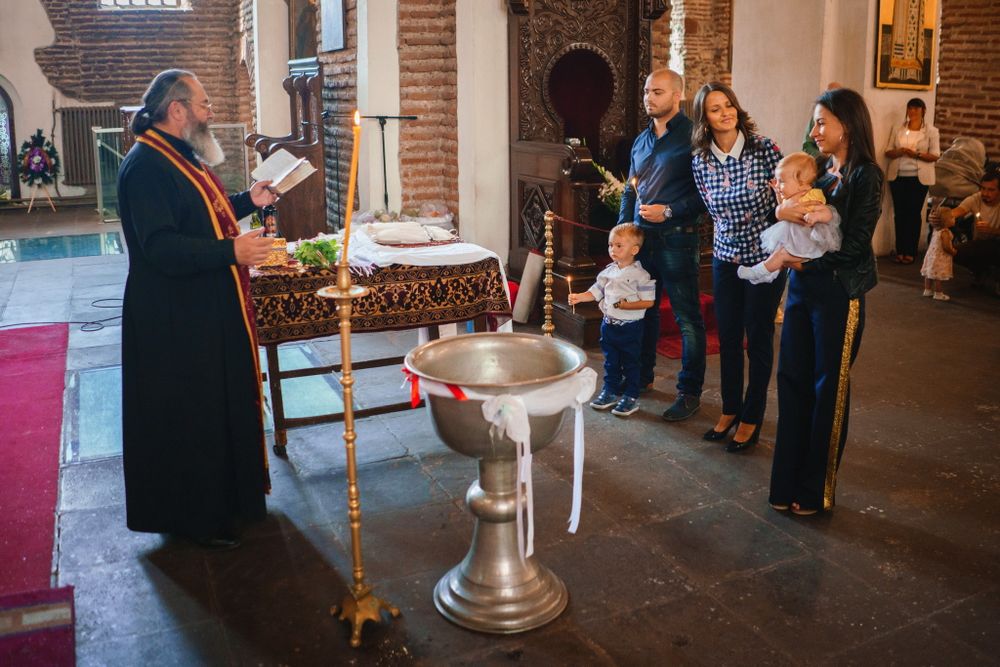 Orthodox baptism ceremony taking place near a traditional font in a church interior.