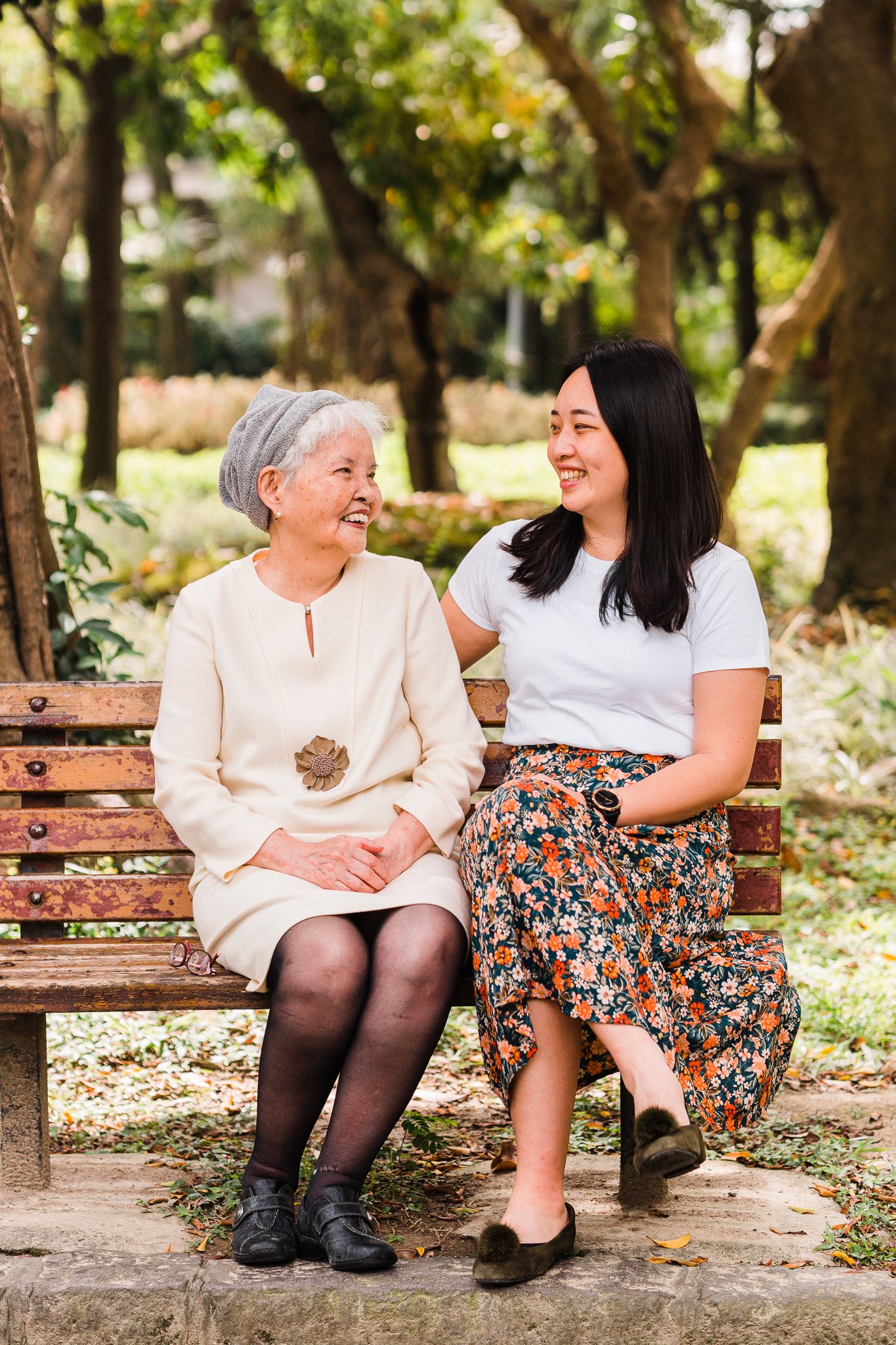 Senior woman and younger woman sharing a warm moment while sitting together on park bench.