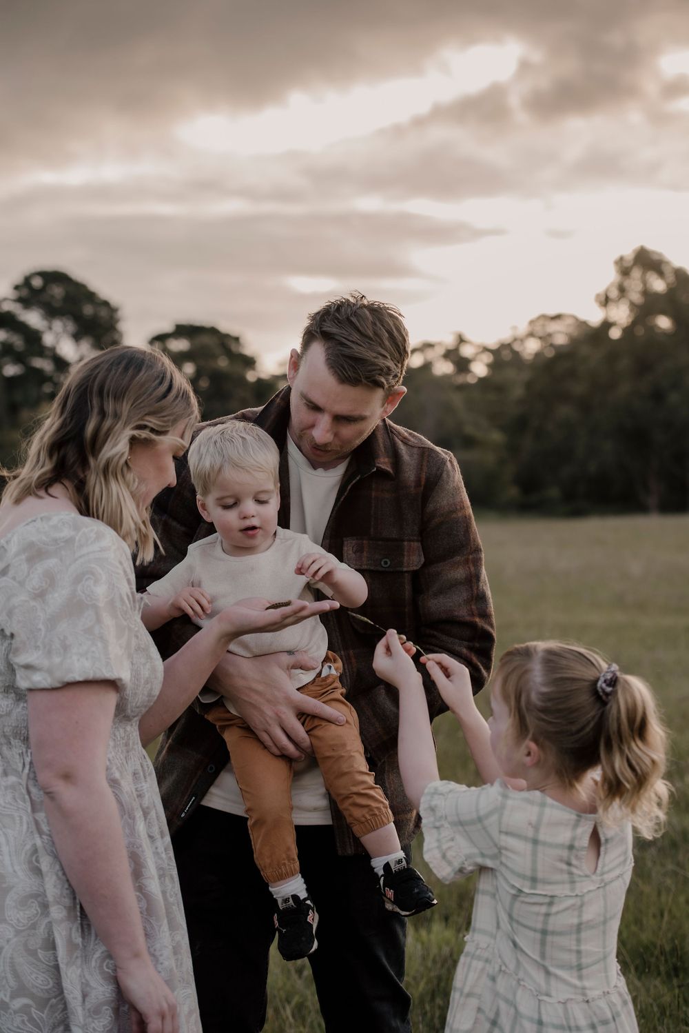 A family shares a tender moment together in a field at sunset with moody skies overhead.
