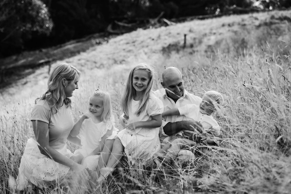 A black and white photograph of a family sitting together in tall grass on a hillside during a sunny afternoon.