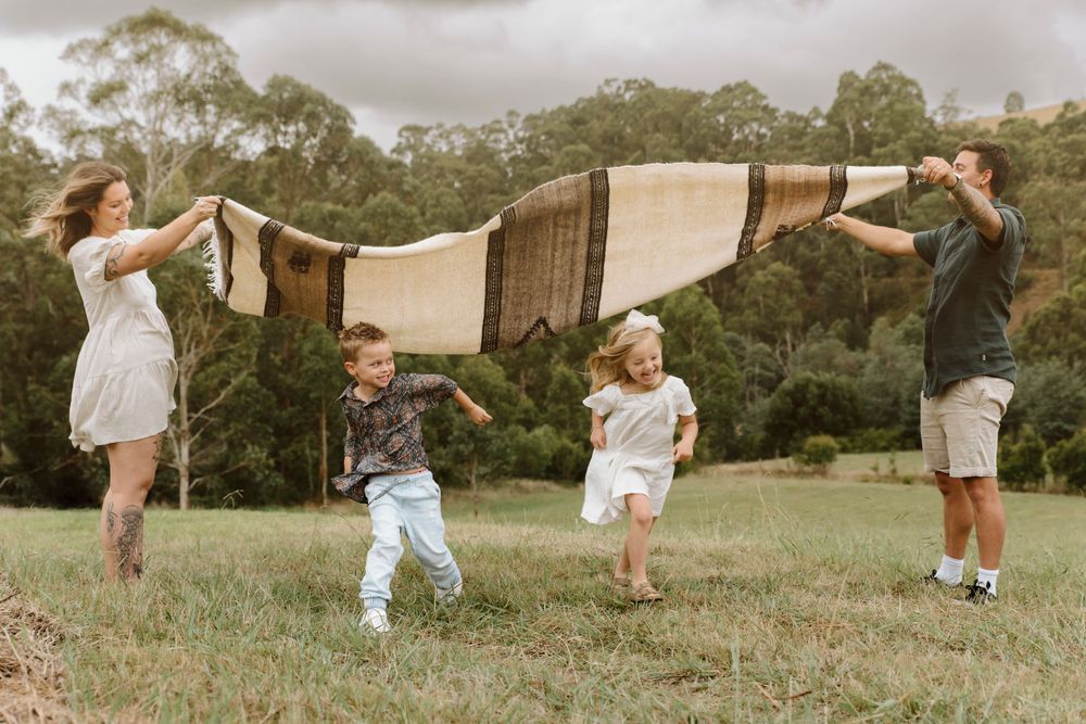 A family stands in a grassy field running under a blanket.
