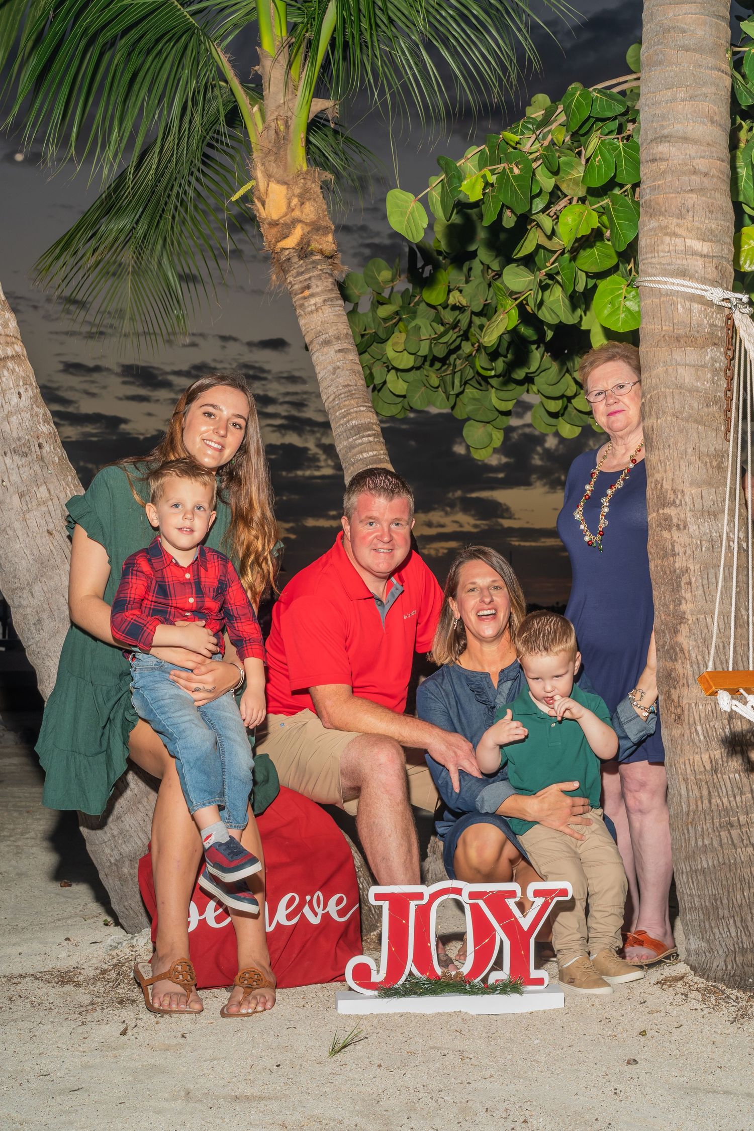 Family sitting together on a beach at night with holiday decorations and palm trees.
