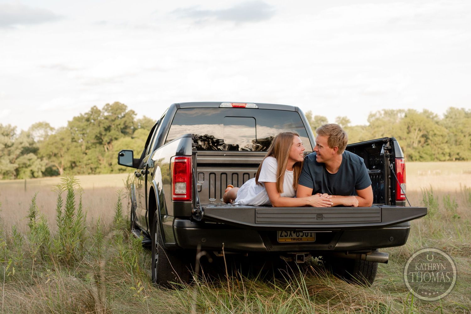 Couple relaxing together in the back of a black pickup truck in a rural field.