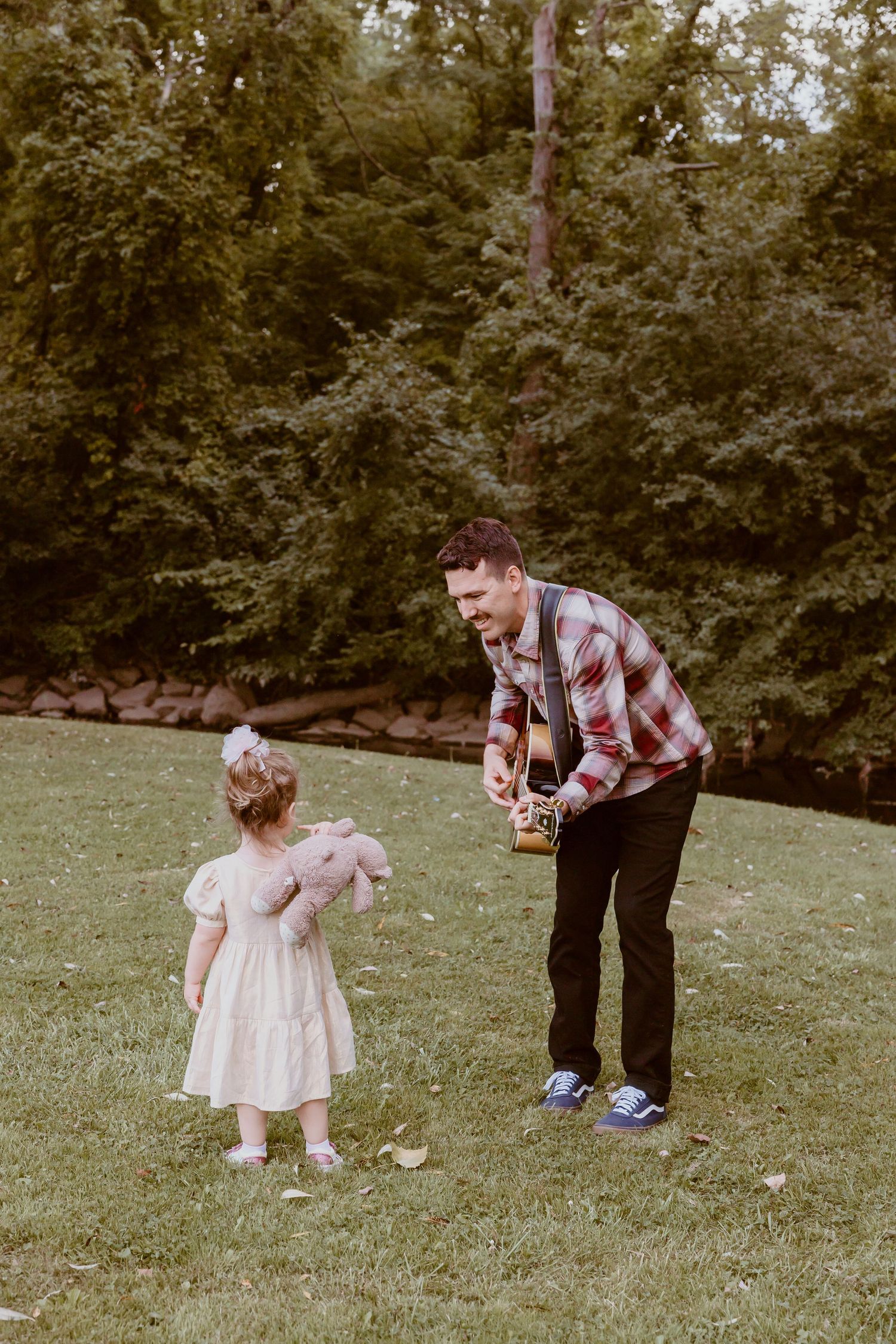 A person teaching a small child in a white dress how to play guitar outdoors.
