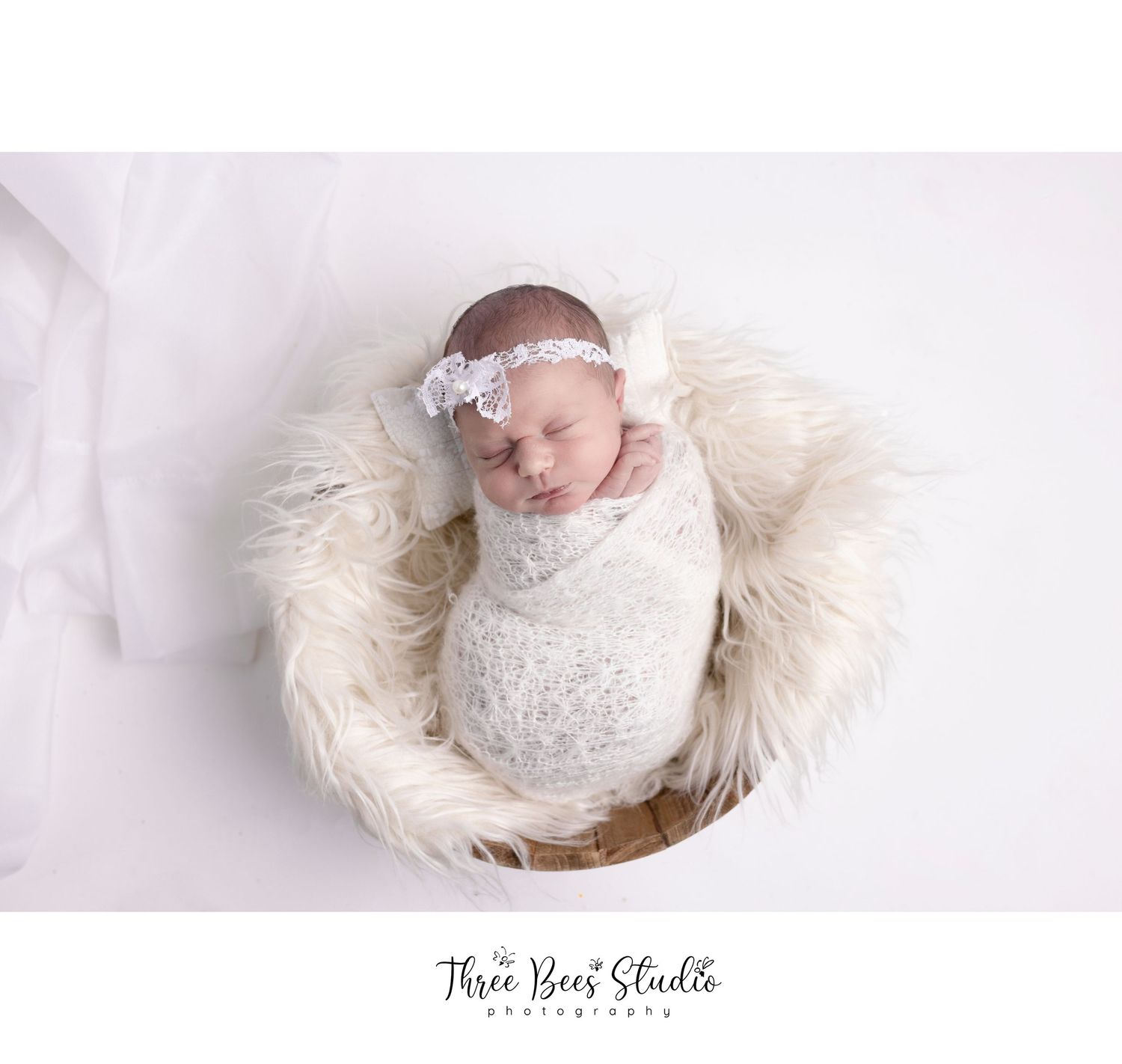Professional newborn portrait in white lace wrap on furry circular backdrop.