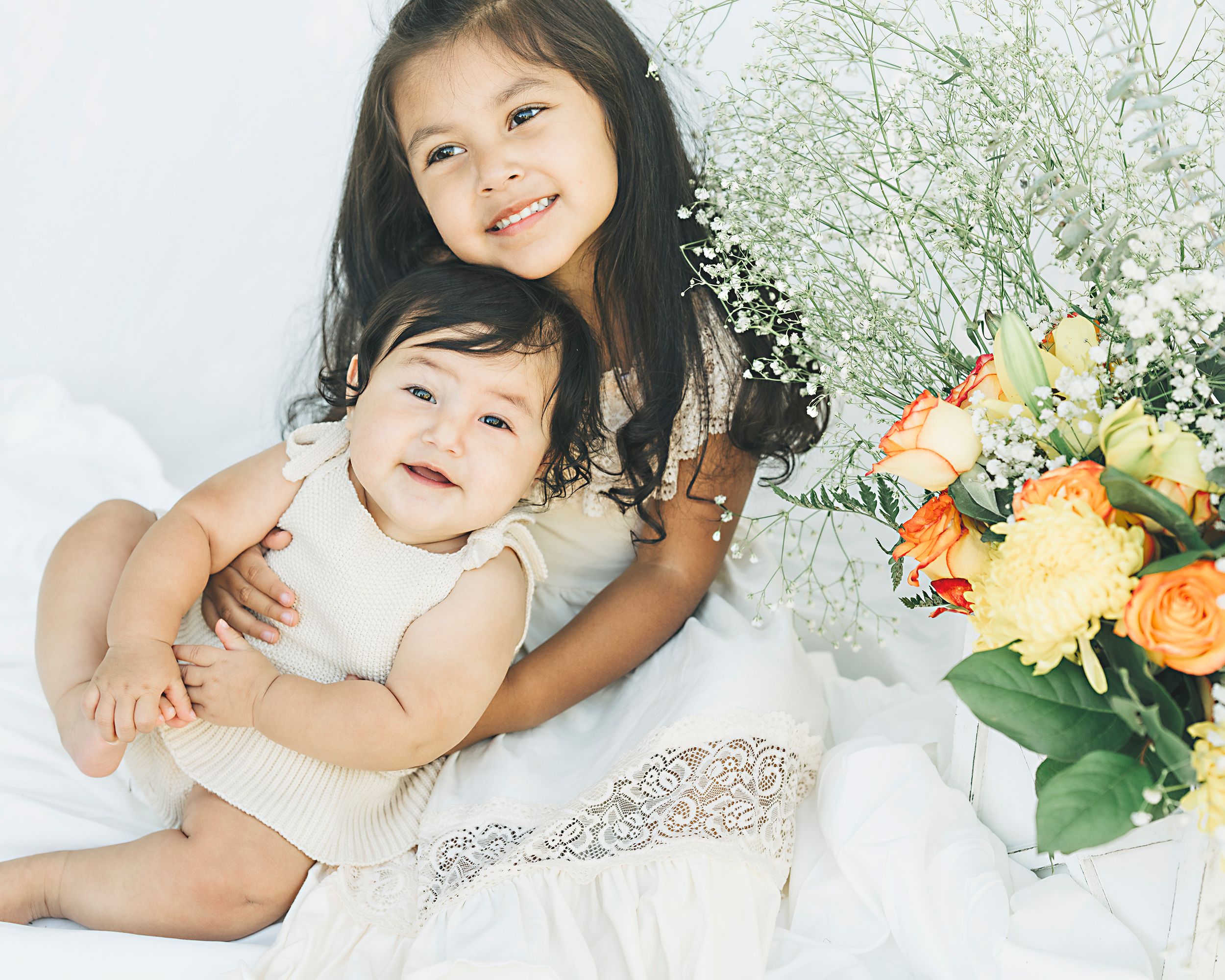 Sweet portrait of two children embracing with orange and yellow flowers in background.