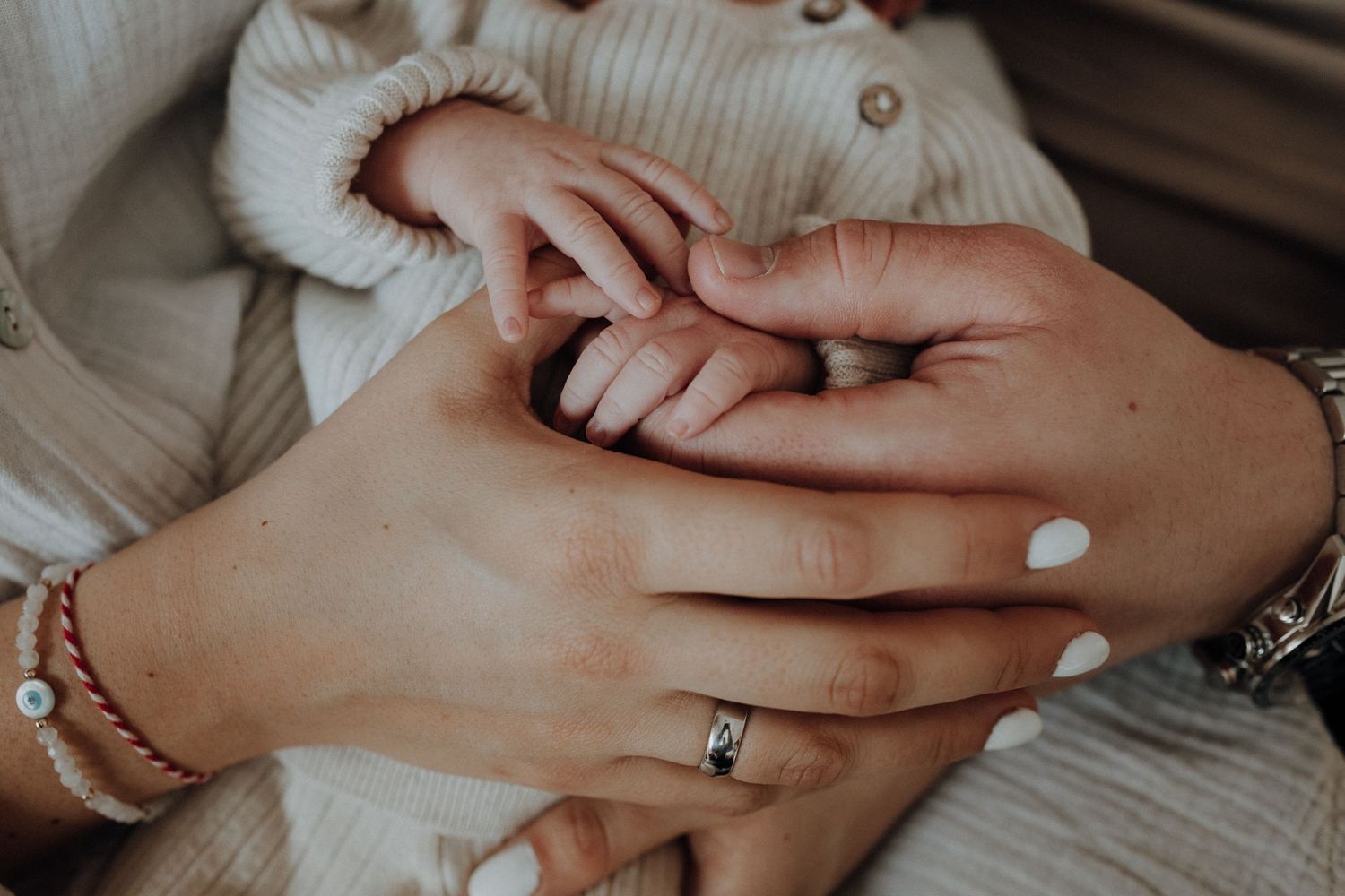 Close-up of a newborn baby's tiny hand held gently by a mother wearing a diamond ring and bracelet.