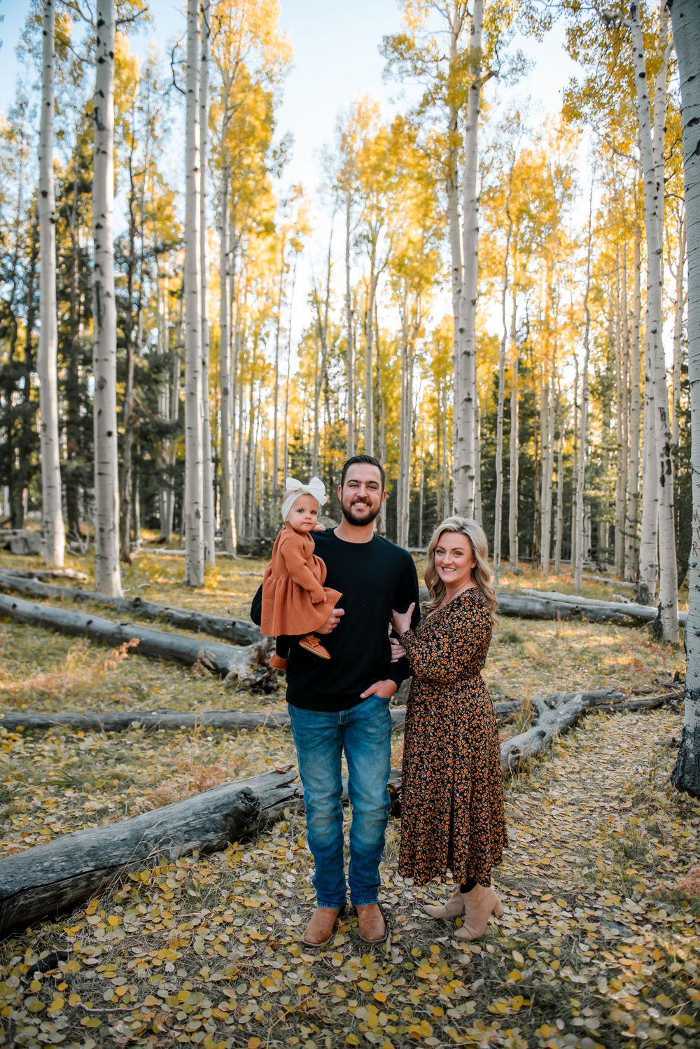Family enjoying a fall photoshoot among tall aspen trees with yellow leaves scattered on the ground.