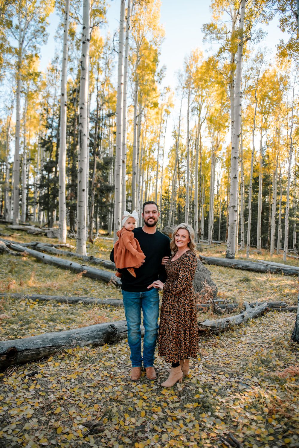 Family portrait session in an autumn aspen forest with golden leaves on the ground.