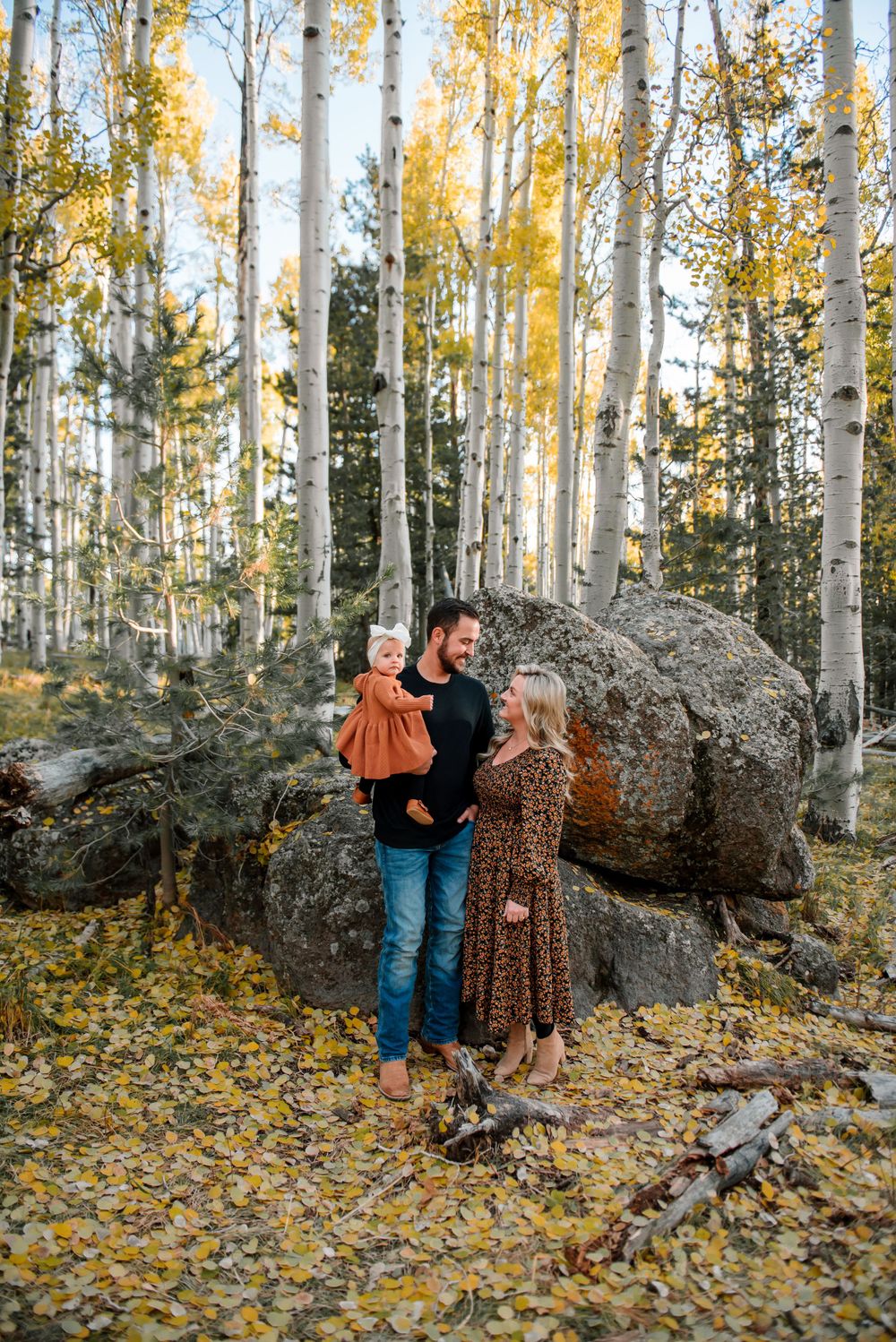 Family poses by large boulder in aspen forest during fall season.
