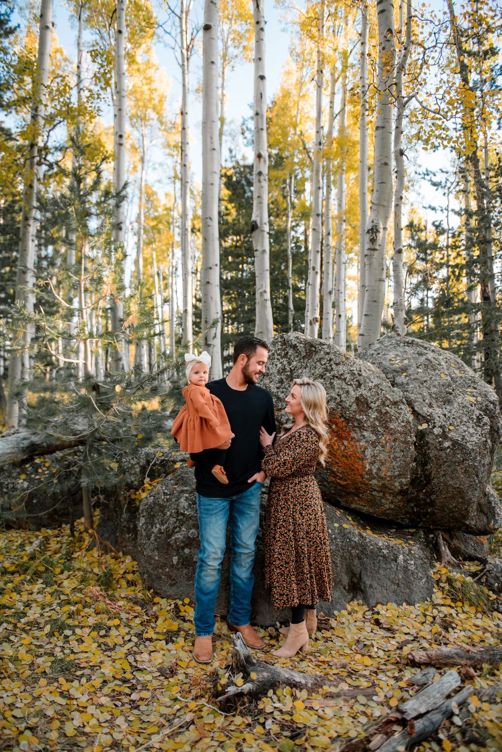 Family shares candid moment together near rocky outcrop in autumn aspen forest.