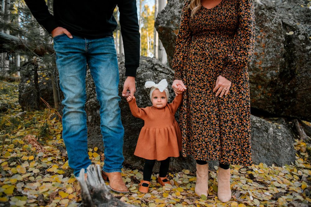 Family photoshoot among aspen trees and boulders with fall foliage on ground.