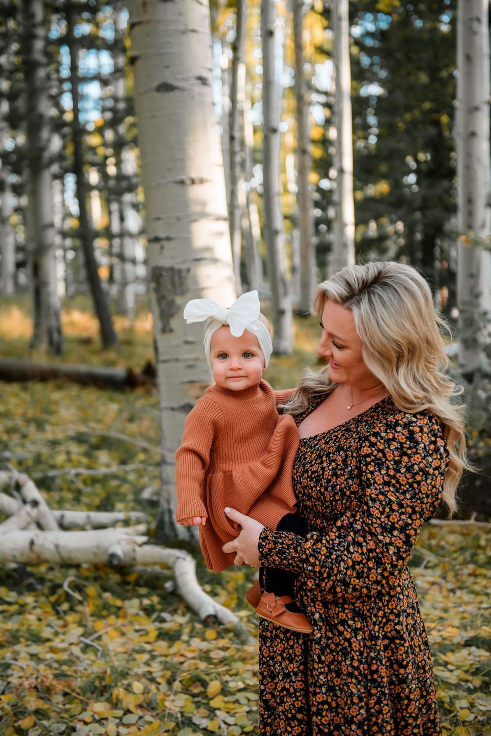 A playful autumn photoshoot in an aspen forest with a floral dress and rust-colored sweater.
