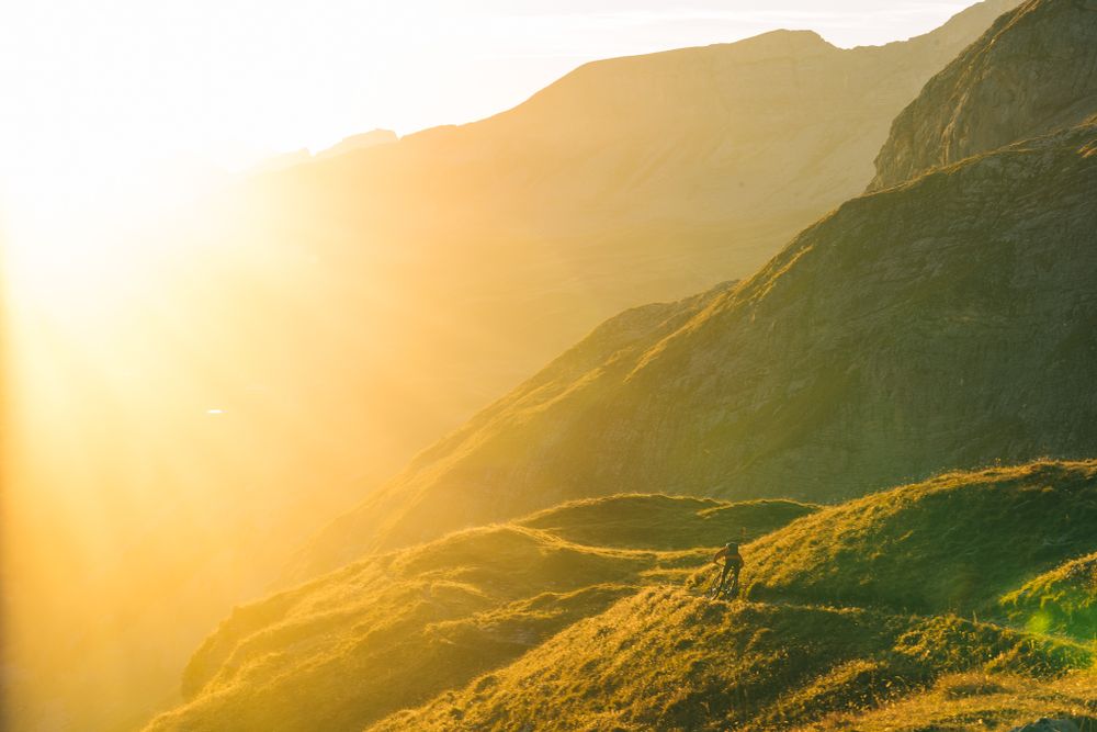 Golden sunlight illuminates misty mountain slopes during sunset in a dramatic alpine landscape.
