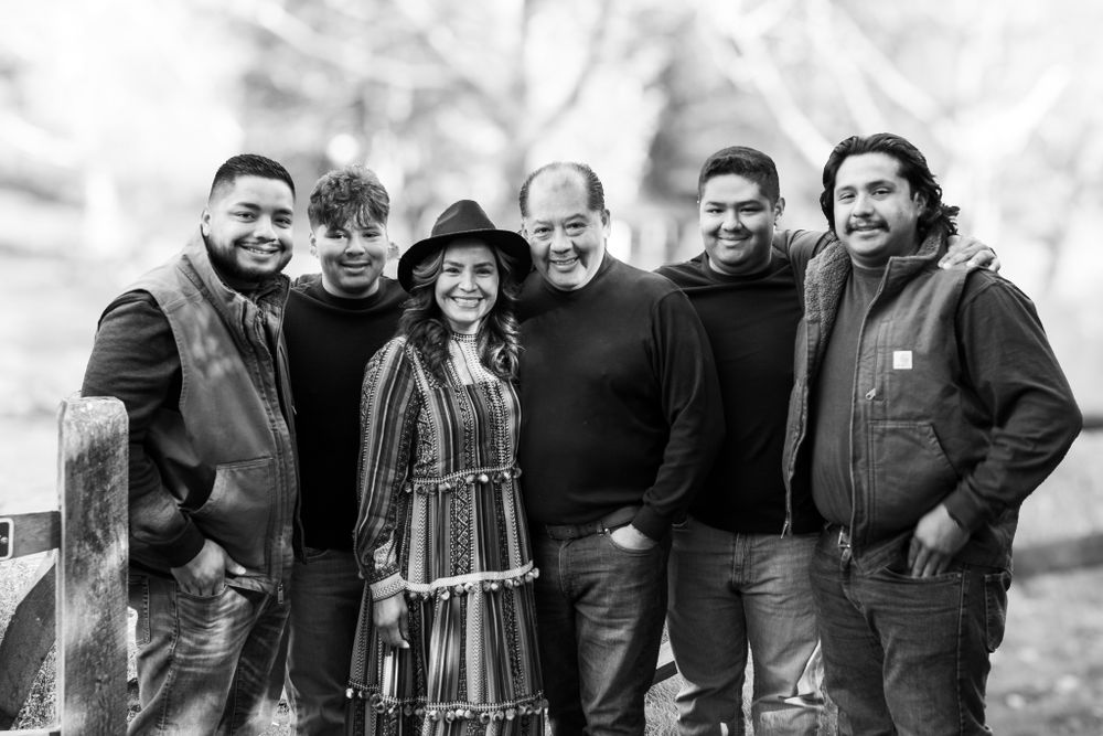 Black and white photo of six people smiling together outdoors in a park setting during autumn.