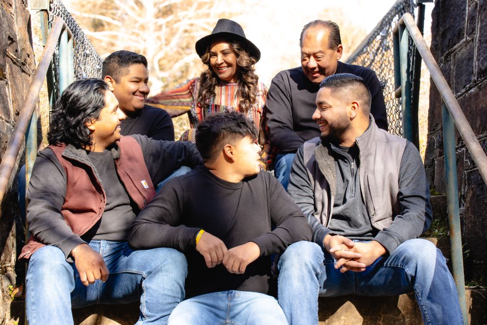 Group of six people sitting and laughing together on outdoor steps in casual autumn attire.