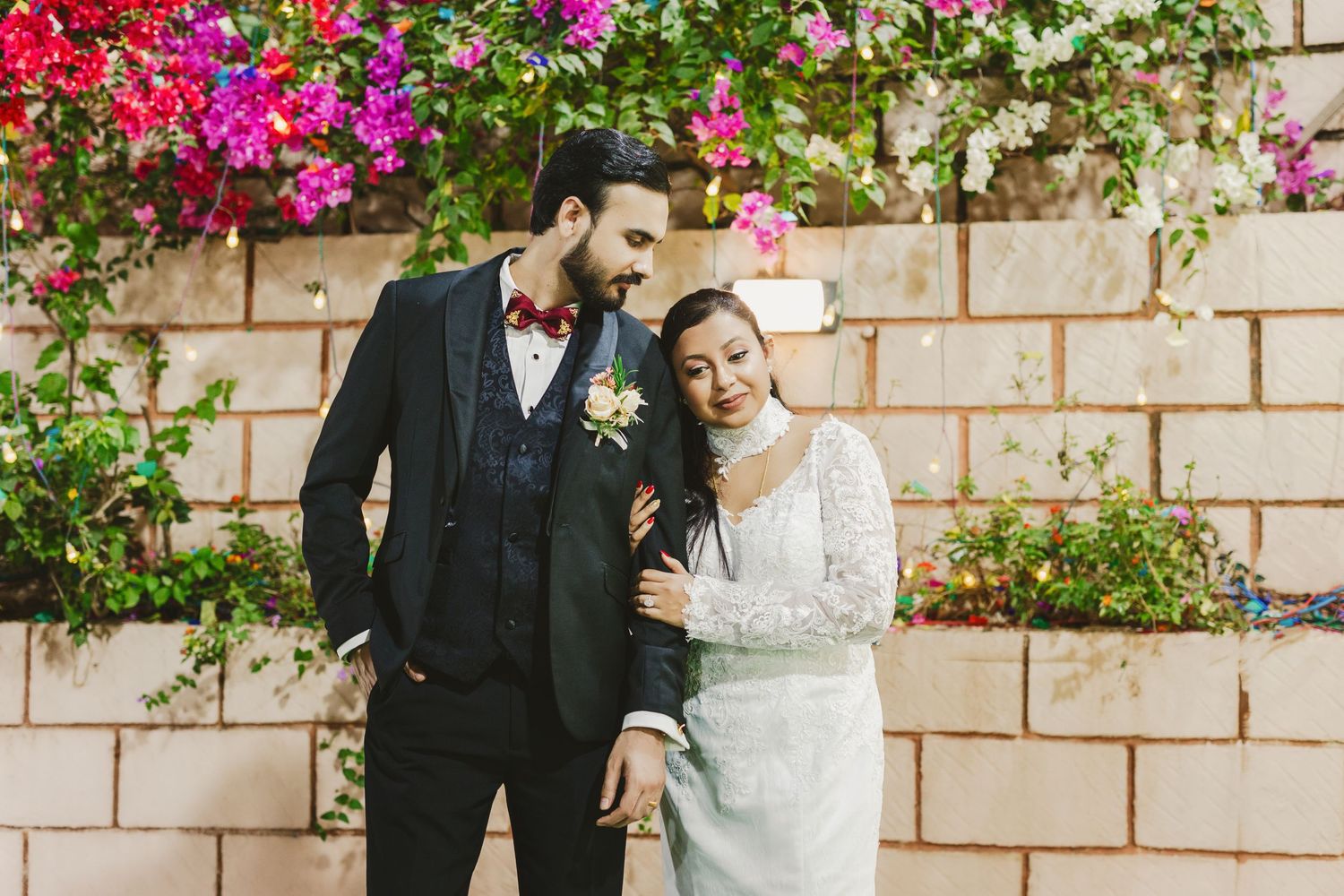 Wedding celebration in front of a stone wall adorned with colorful flowering vines.