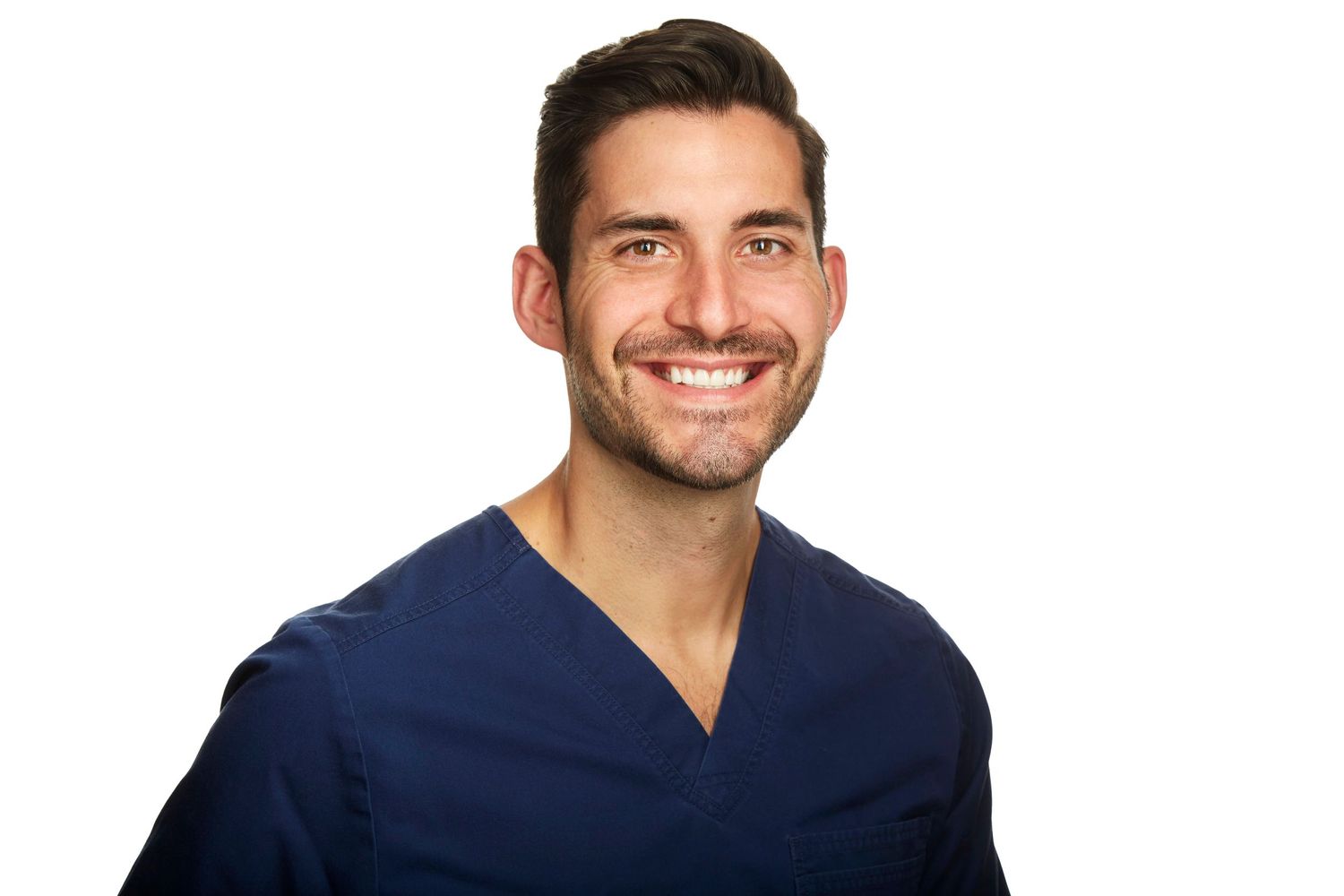 A healthcare professional wearing navy blue scrubs smiles warmly against a white background.