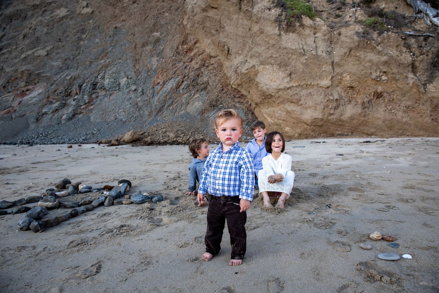 Family portrait on the beach with the youngest of four standing firm in front of the others. J.Perlman Photography previous wedding couple