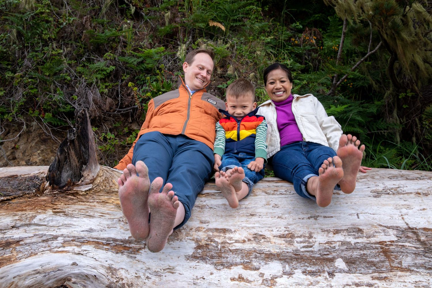 fun family photo sitting on driftwood with their feet forward being silly at Big River beach Mendocino. J.Perlman Photography wedding couple