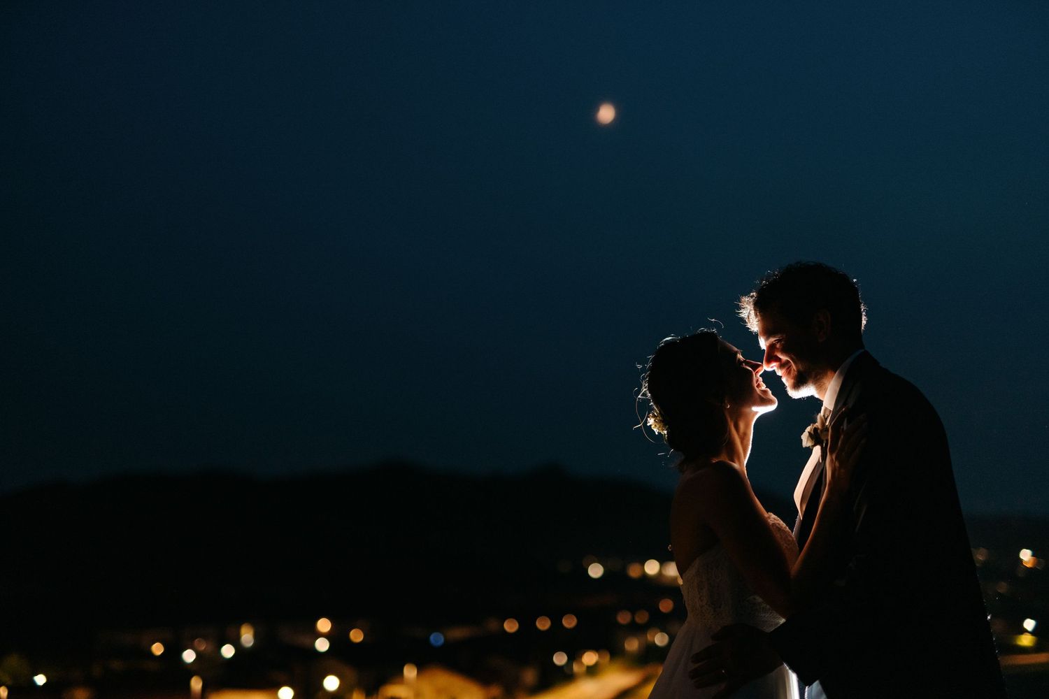 Silhouetted couple shares a romantic moment against a twilight sky with city lights below.