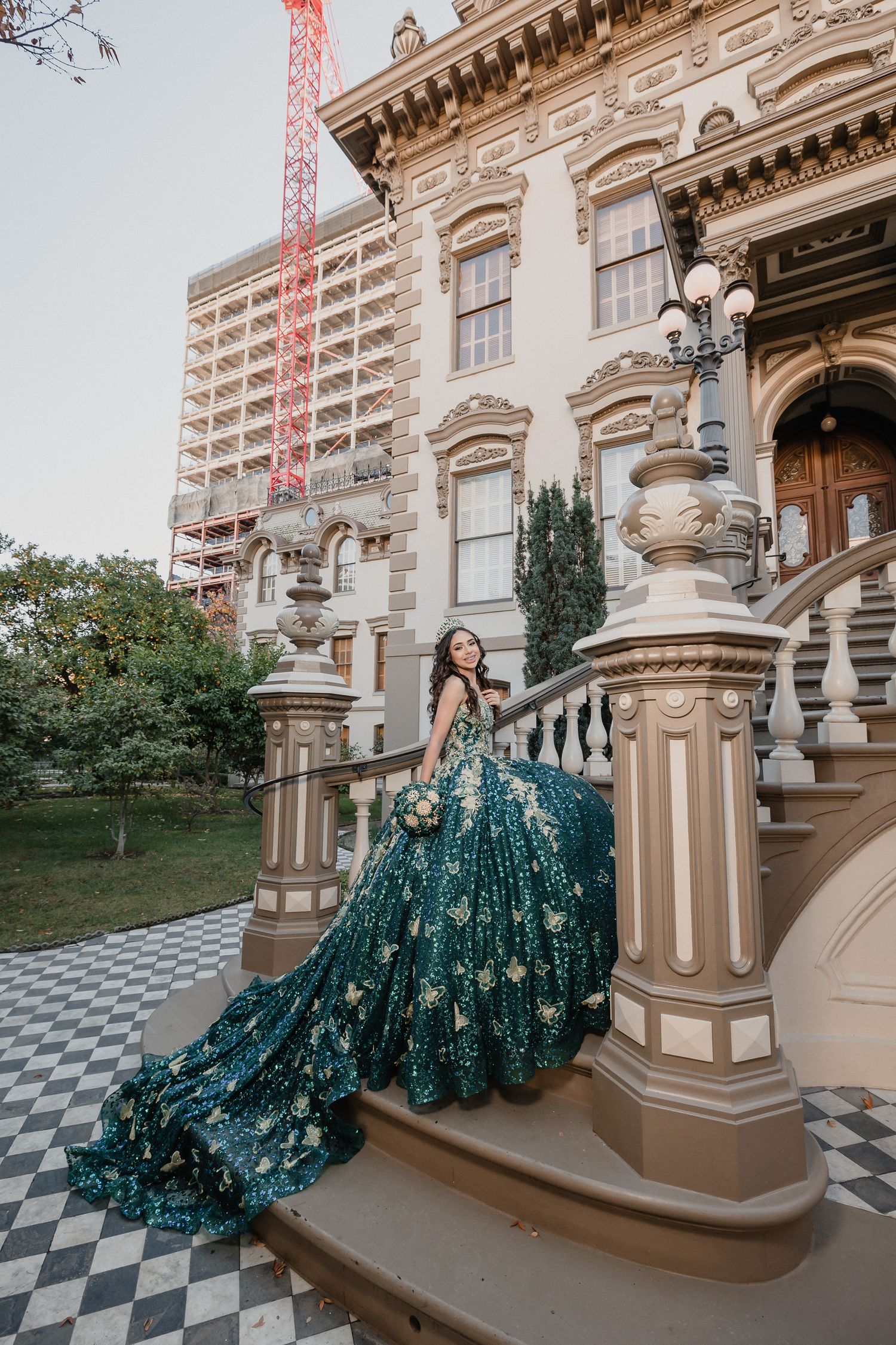 Sparkling teal ballgown with dramatic train flows down ornate stone steps of historic building.