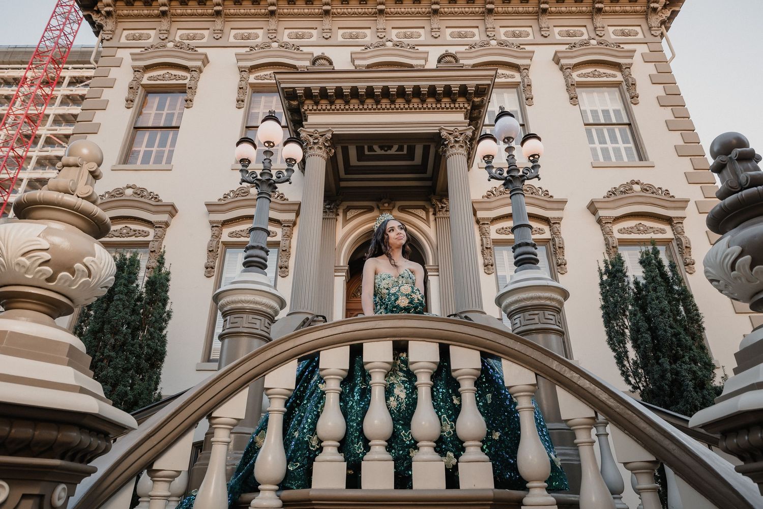 Woman in teal ballgown poses on architectural staircase of historic building.