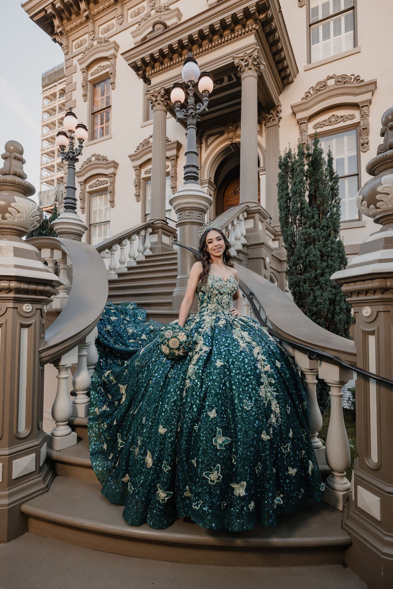 Teal and silver quinceañera ball gown showcased on ornate marble staircase with decorative lamp posts.