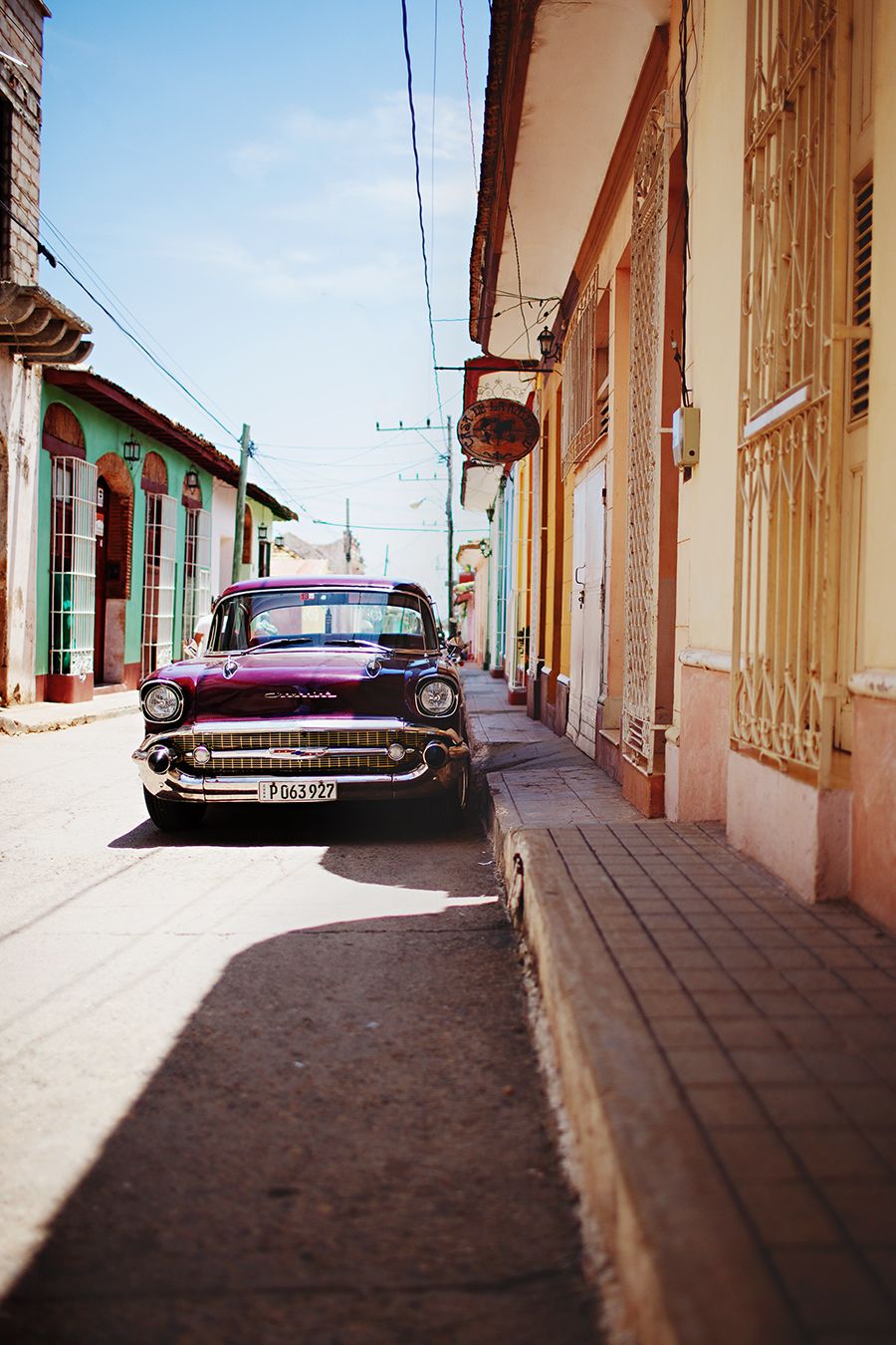 Classic vintage cars parked along a colonial street with pastel-colored buildings.