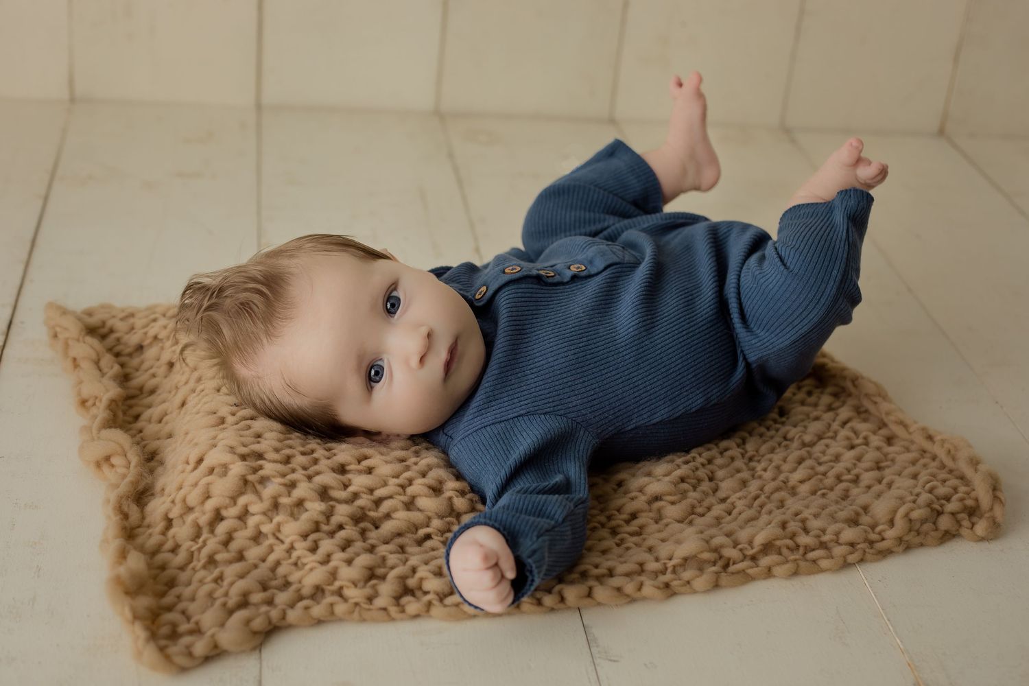 A three month old baby boy wearing blue with a wooden background for his three month milestone photoshoot.
