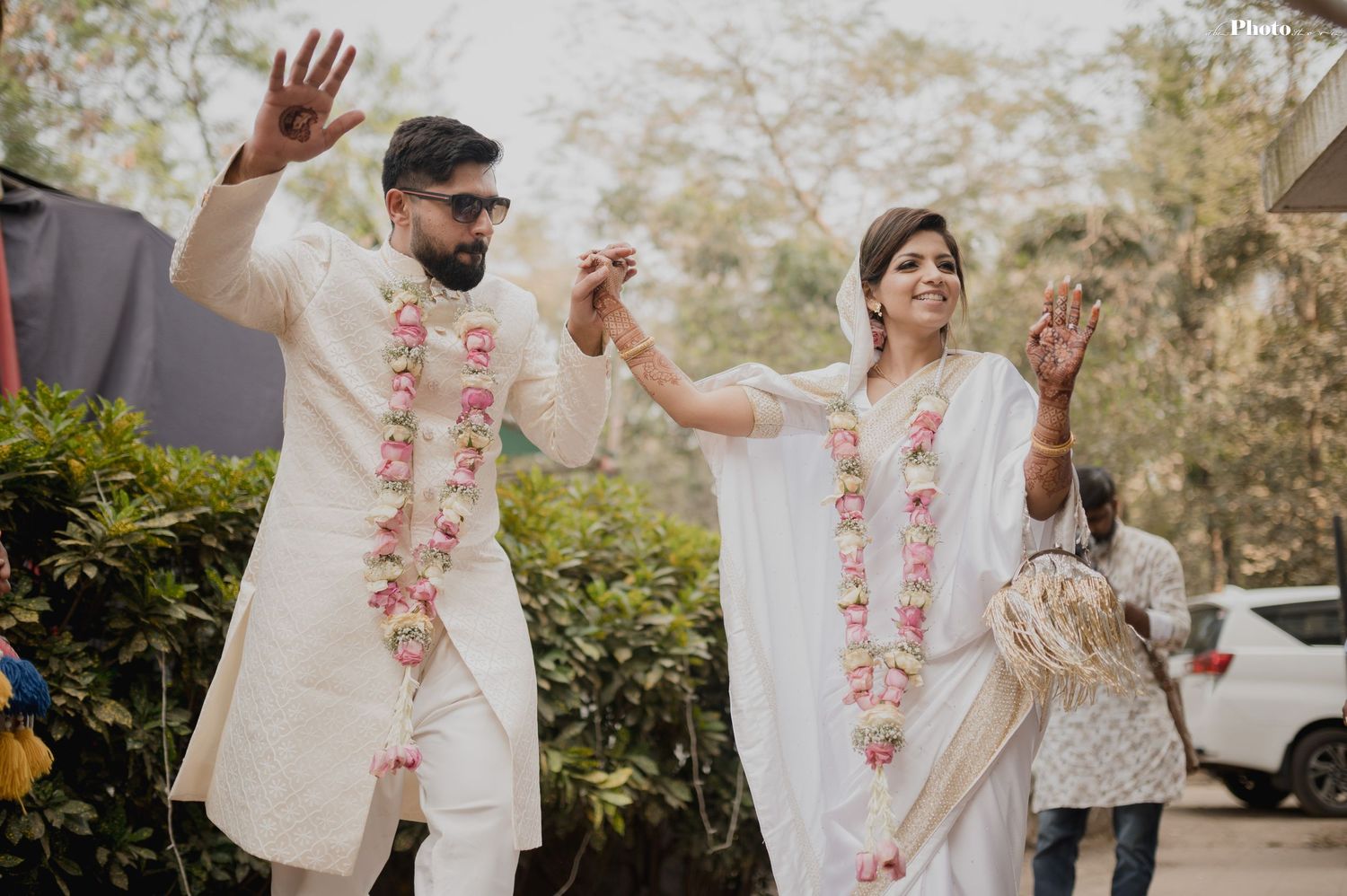 Couple in matching white outfits and floral garlands dance together during outdoor celebration.