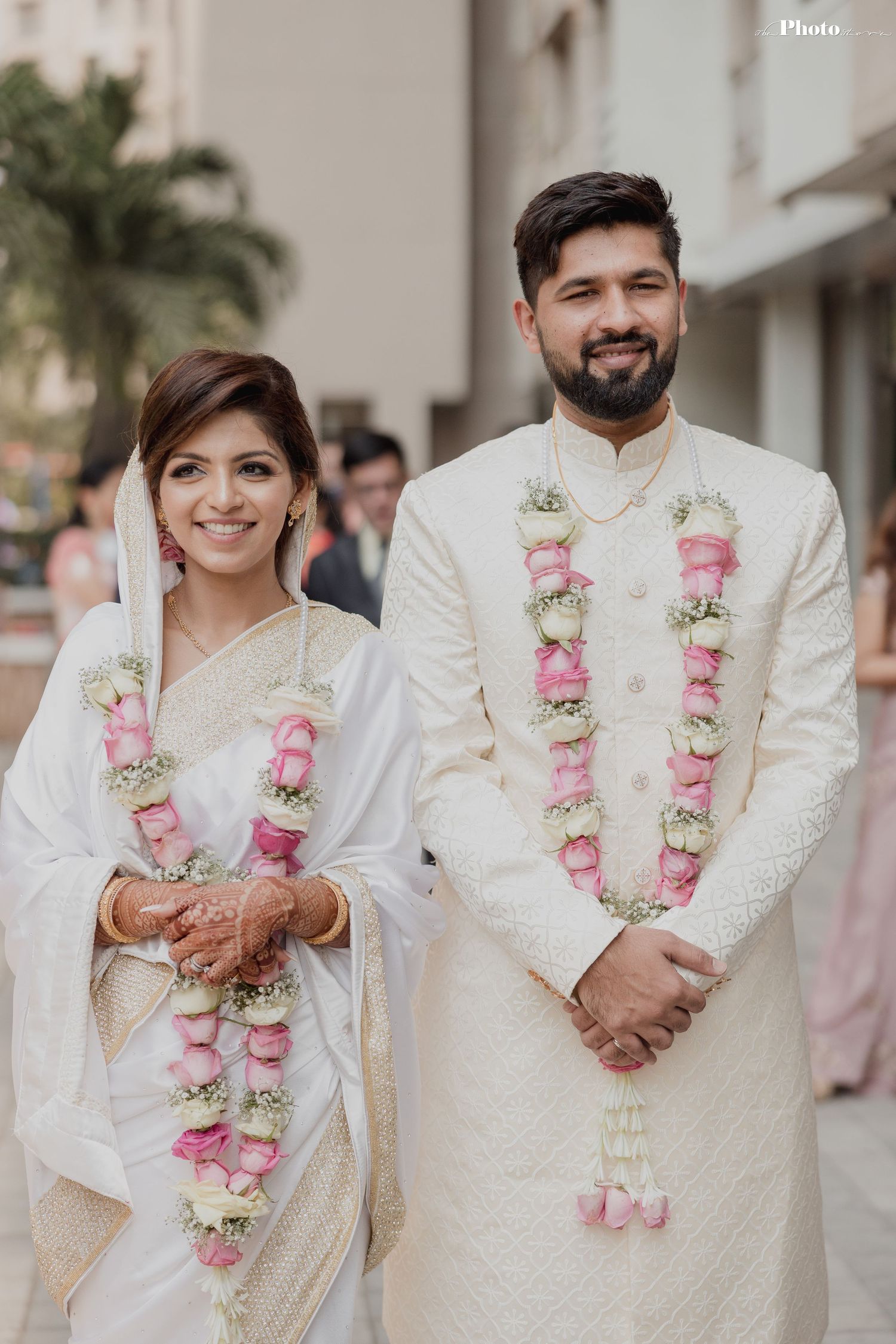 Traditional wedding ceremony with couple wearing white outfits and pink floral garlands.