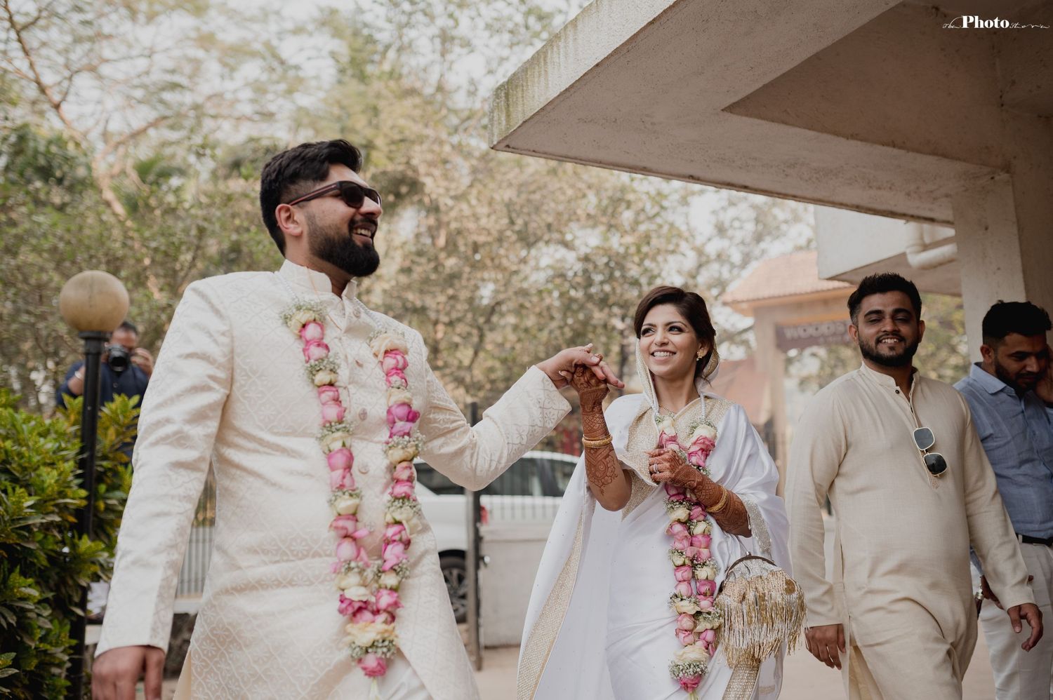 A couple in elegant white attire celebrates their special day in a garden setting.