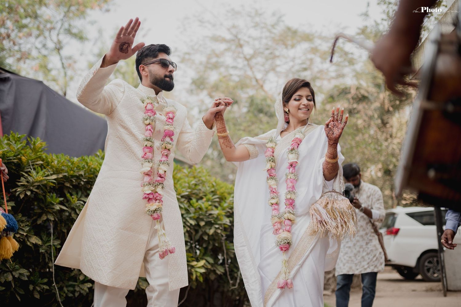 A couple in white wedding outfits shares joyful moments during their outdoor celebration.