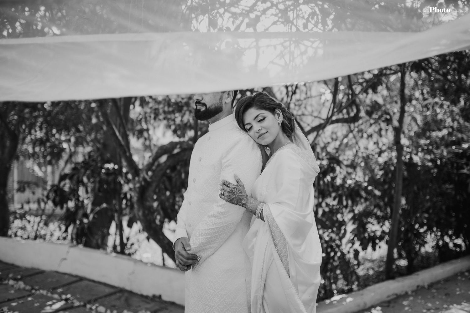 A black and white photo captures a couple in white wedding attire sharing a tender moment.