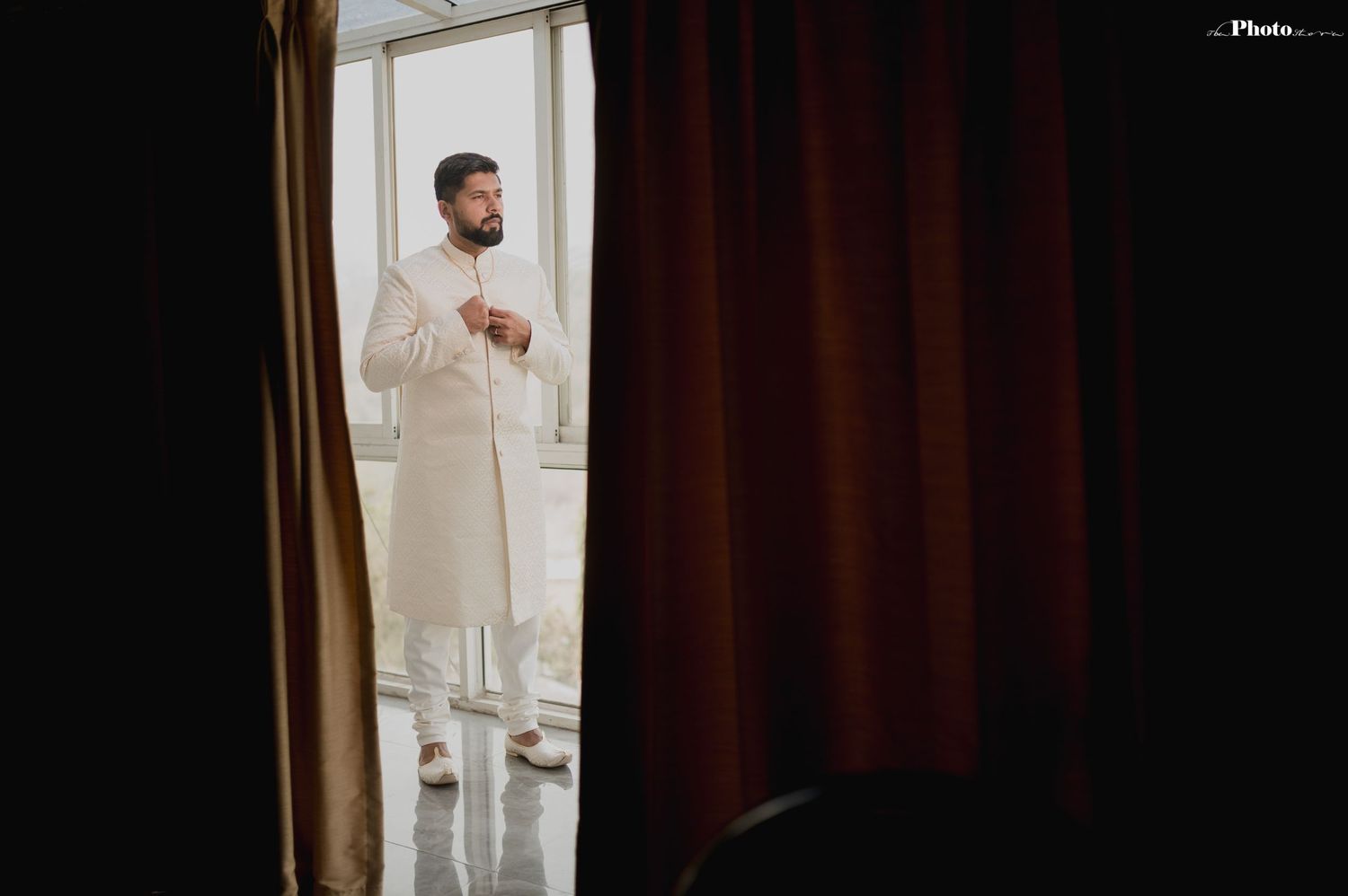 Elegant figure in white attire photographed through curtained doorway.