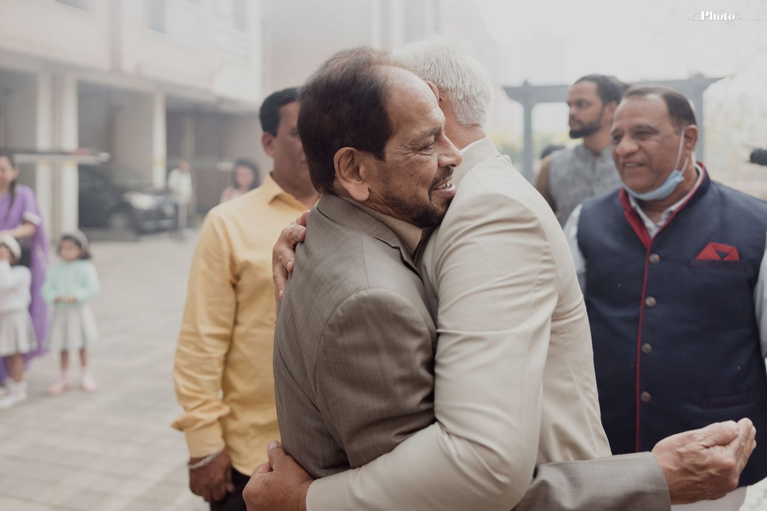 Guests in formal attire share warm embraces at an outdoor gathering.