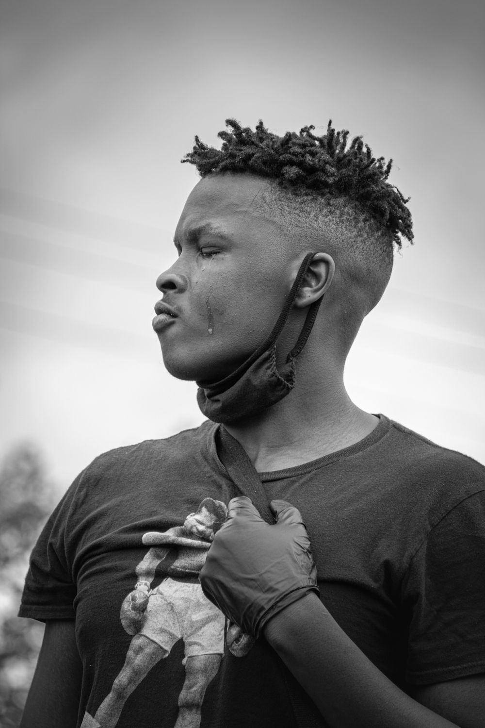 Black and white portrait of young man with dreadlocks wearing mask pulled down around chin.