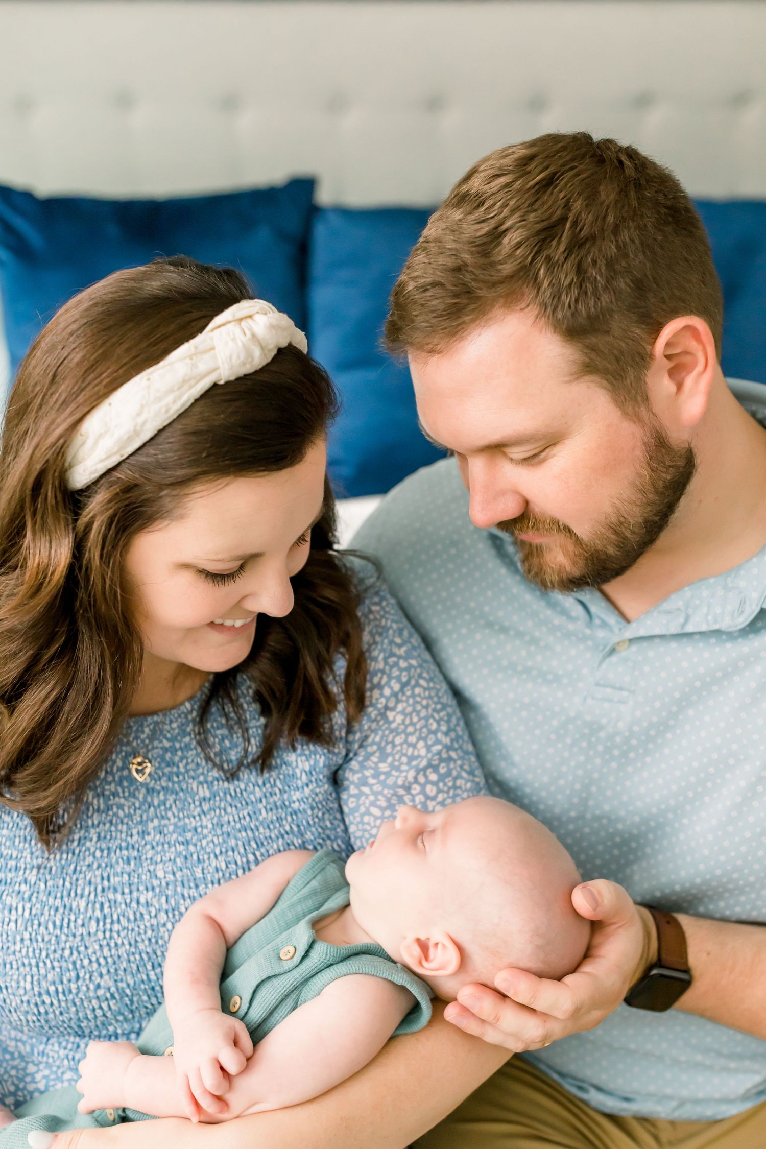 An intimate family moment on a white bed with bright blue accent pillows and soft natural lighting.