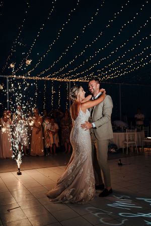A romantic first dance under twinkling string lights with sparkler effects creating a magical atmosphere.