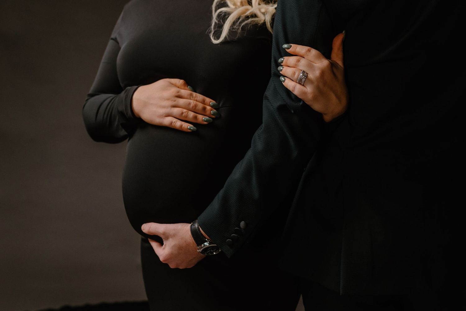 Close-up view of hands cradling a pregnant belly against dark clothing.
