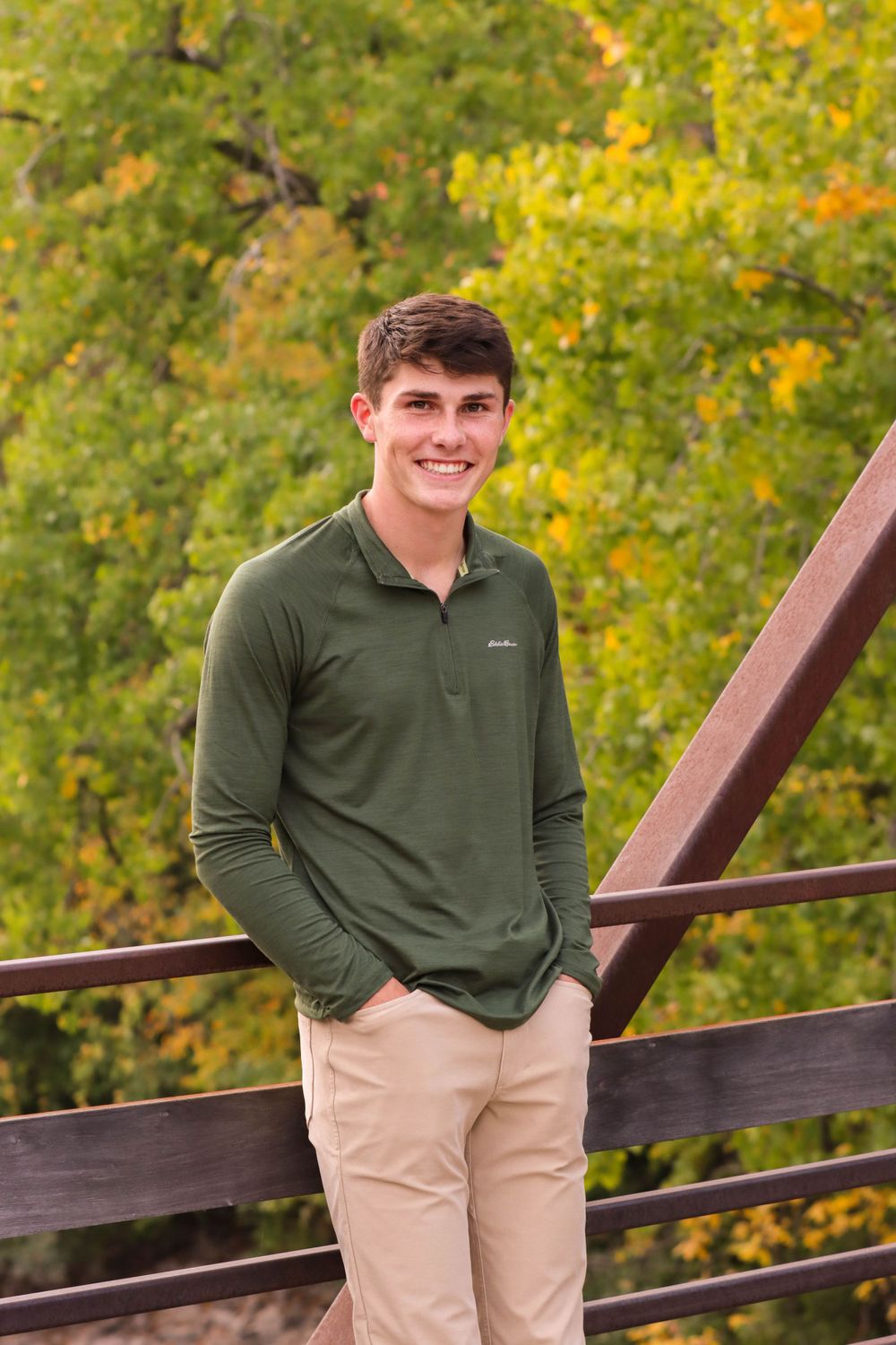 Person in green polo shirt stands on wooden bridge with autumn foliage in background.