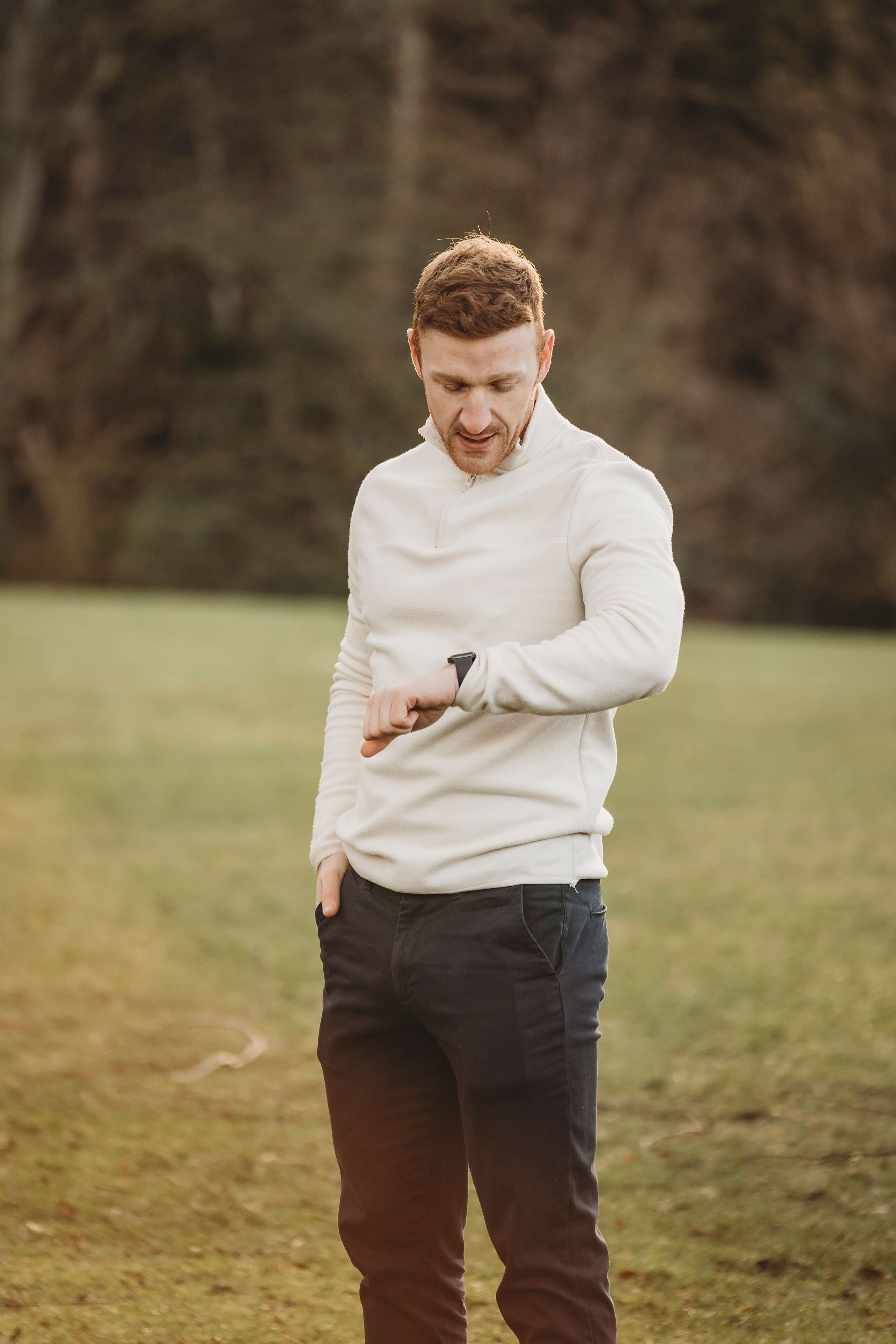 Athletic person in white sweater checking smartwatch in outdoor setting.