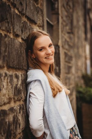 Portrait of person in white sweater smiling against historic stone wall.