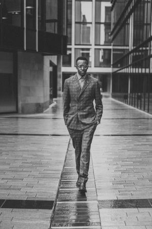 Professional in plaid suit walking confidently through modern building courtyard.