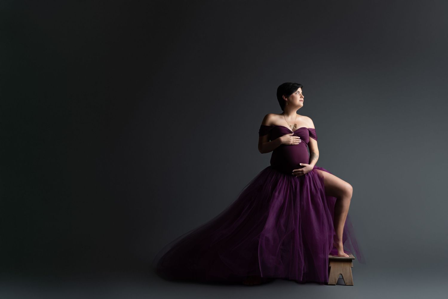Dramatic maternity portrait with woman in flowing purple gown against dark background.